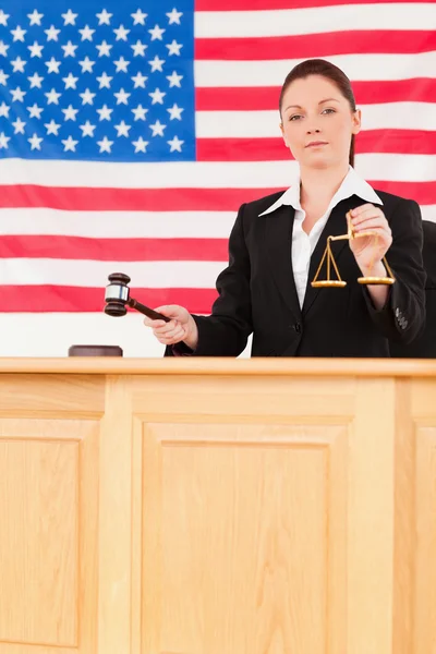 Young judge knocking a gavel and holding scales of justice — Stock Photo, Image