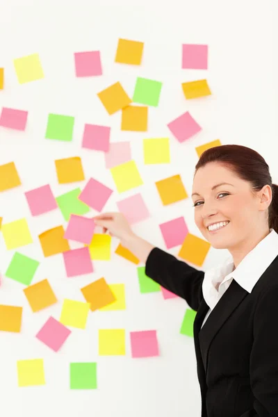 Mujer sonriente poniendo notas reposicionables en una pared blanca —  Fotos de Stock