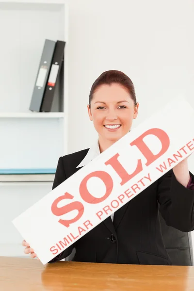 Young real estate agent holding a sold placard — Stock Photo, Image