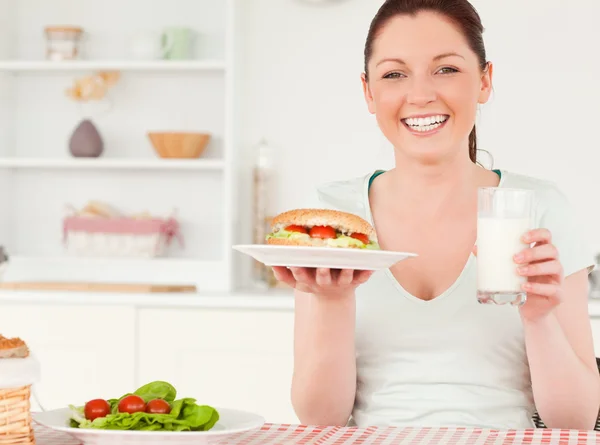 Bir sandviç tutan genç bir kadın ve bir bardak süt gülüyor — Stok fotoğraf