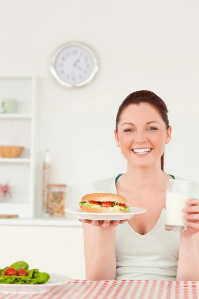Porträtt av en skrattande ung kvinna med en smörgås och ett glas — Stockfoto