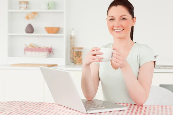 Attraktive Frau entspannt auf ihrem Laptop, während sie eine Tasse Kaffee trinkt — Stockfoto