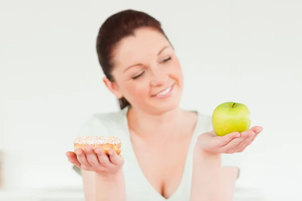 Красивая женщина позирует, держа в руках пончик и зеленое яблоко — стоковое фото