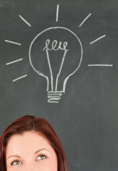 Beautiful young woman with a bulb draw on a blackboard in the ba — Stock Photo, Image