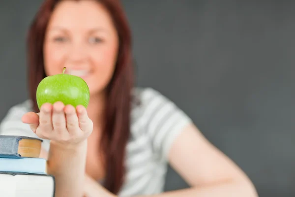 Cute student showing an apple with the camera focus on the fruit — Stock Photo, Image
