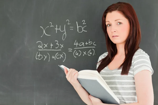 Cute woman trying to solve a mathematical equation on a blackboa — Stockfoto