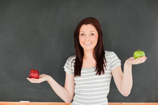 Leuke vrouw met een appel aan elke hand tegen een schoolbord — Stockfoto
