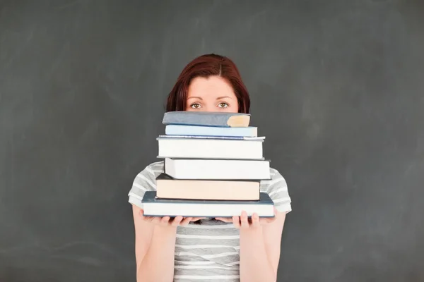 Carina giovane donna nascondersi dietro una pila di libri — Foto Stock