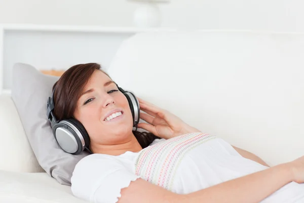 Dość brunetka kobieta relaksując się przy jej słuchawki leżąc — Zdjęcie stockowe