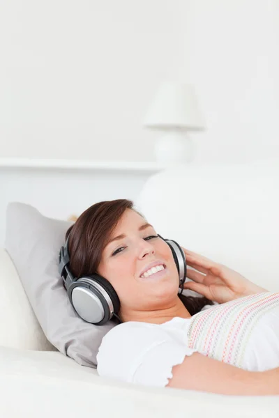 Uroczy, brunetka kobiece relaks z jej słuchawki podczas lyin — Zdjęcie stockowe