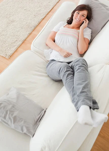 Mulher morena adorável ao telefone enquanto deitada em um sofá — Fotografia de Stock