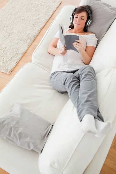 Junge schöne Frau liest ein Buch, während sie auf einem Sofa liegt — Stockfoto