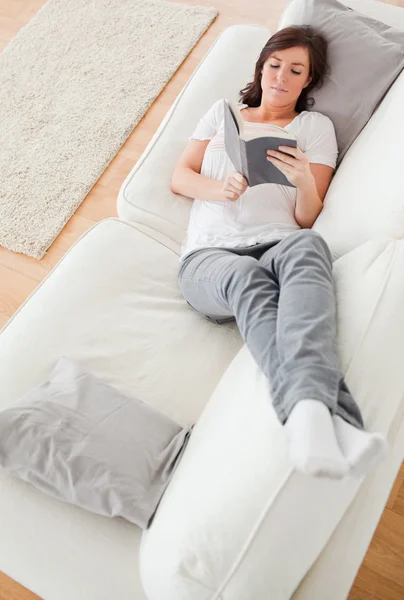 Młoda kobieta szuka dobry, czytając książkę leżąc na kanapie — Zdjęcie stockowe