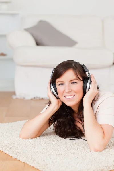 Wspaniały brunetka dama przy użyciu słuchawek, leżąc na dywanie — Zdjęcie stockowe