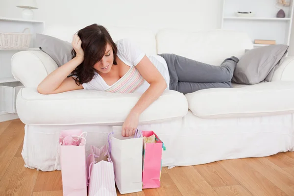 Jovem mulher bonito posando com seus sacos de compras enquanto deitado em um — Fotografia de Stock