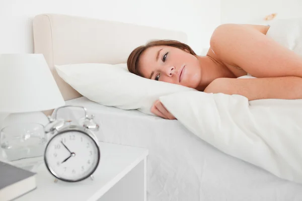 Όμορφη μελαχρινή γυναίκα ξύπνημα με ένα ρολόι ενώ βρίσκεται — Φωτογραφία Αρχείου