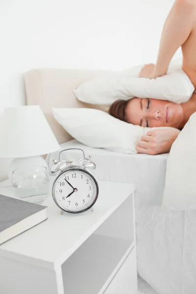 Cute brunette woman awaking with a clock while lying — Stock Photo, Image