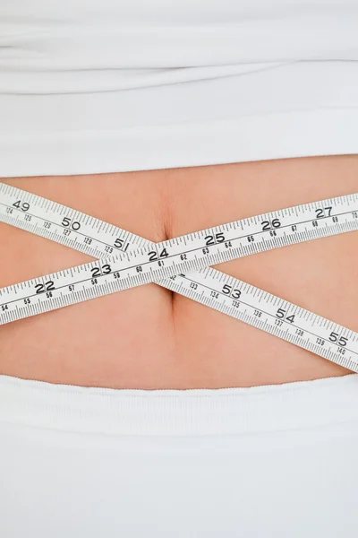 Mujer joven midiendo su vientre con una cinta métrica mientras está de pie —  Fotos de Stock