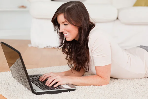 Atrakcyjny brunetka dama relaksując się przy jej laptop podczas leżącego o — Zdjęcie stockowe