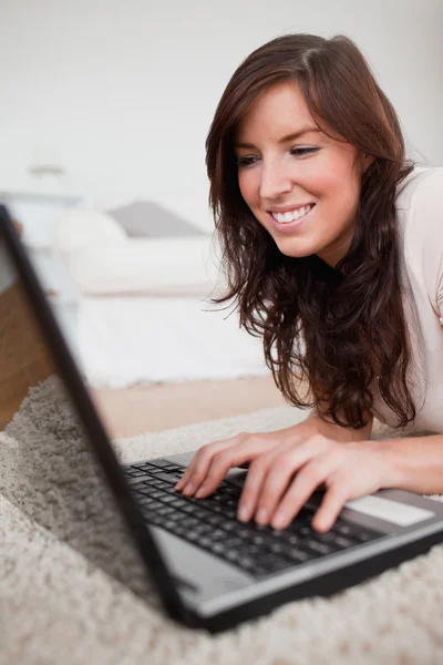 Lockande brunett kvinna avkopplande med sin laptop liggande — Stockfoto