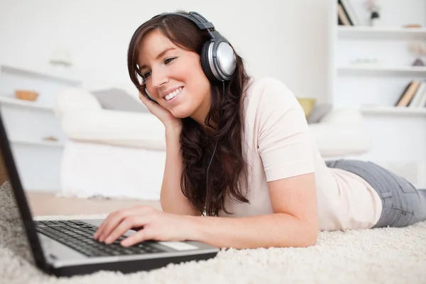 Dość brunetka kobiece relaks z jej laptop leżąc na — Zdjęcie stockowe
