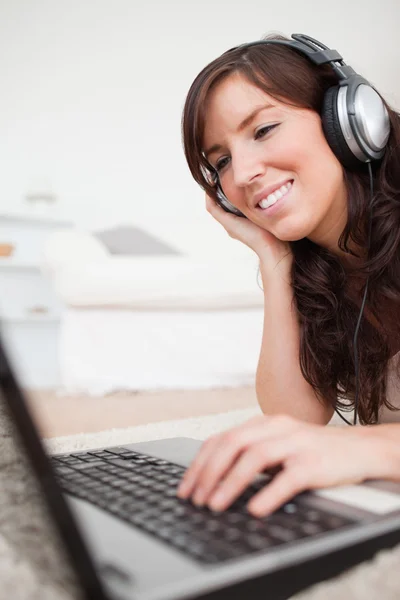 Sorridente bruna femminile rilassante con il suo computer portatile mentre sdraiato su — Foto Stock