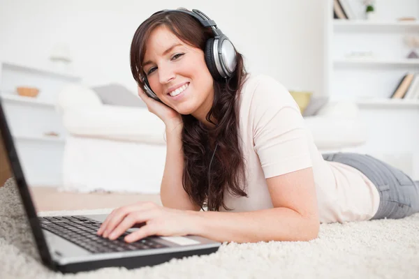 Gelukkig brunette vrouwelijke ontspannen met haar laptop terwijl liggend op een — Stockfoto