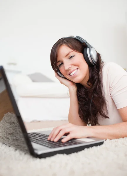 Wesoła brunetka kobieta relaksując się przy jej laptop leżąc na — Zdjęcie stockowe