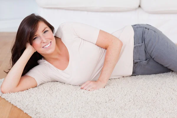 Mulher sorridente bonita posando enquanto deitado em um tapete — Fotografia de Stock