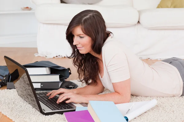 Junge glückliche Frau entspannt mit ihrem Laptop, während sie auf einem Karpfen liegt — Stockfoto