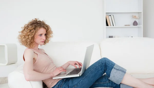 Beautiful blonde woman relaxing with her laptop while sitting on — Stock Photo, Image