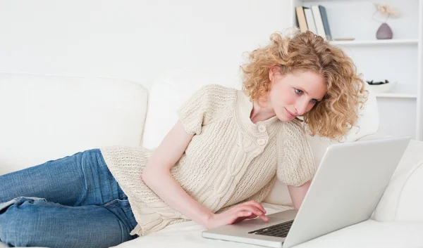 Cute blonde woman relaxing with her laptop while lying on a sofa — Stock Photo, Image