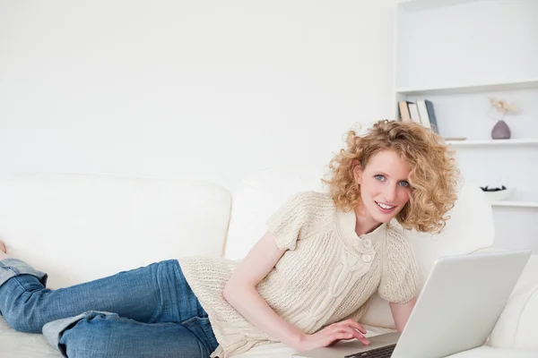 Charmante femme blonde se détendre avec son ordinateur portable tout en étant couché sur un — Photo