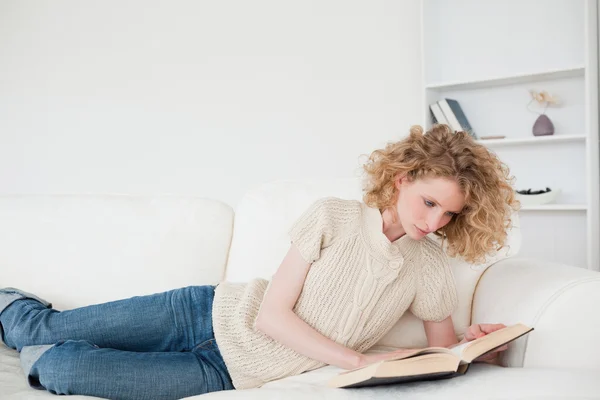 Mooie blonde vrouw lezen van een boek terwijl liggend op een sofa — Stockfoto