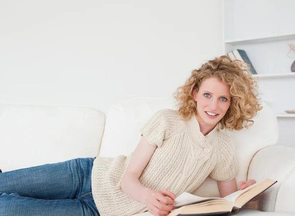 Добре виглядає блондинка читає книгу, лежачи на дивані — стокове фото
