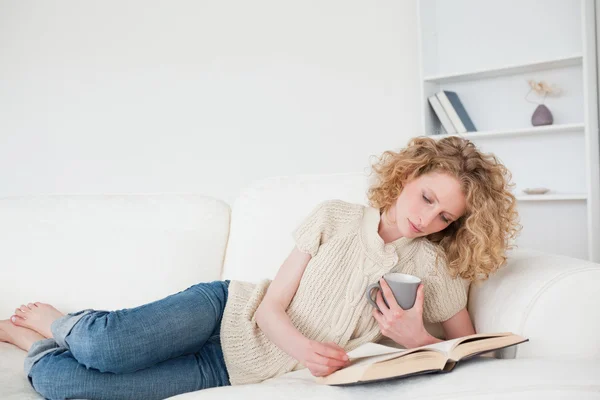 Mulher loira bonita lendo um livro e segurando uma xícara de café w — Fotografia de Stock