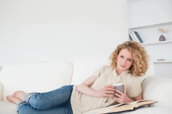 Schöne blonde Frau liest ein Buch und hält eine Tasse Kaffee — Stockfoto