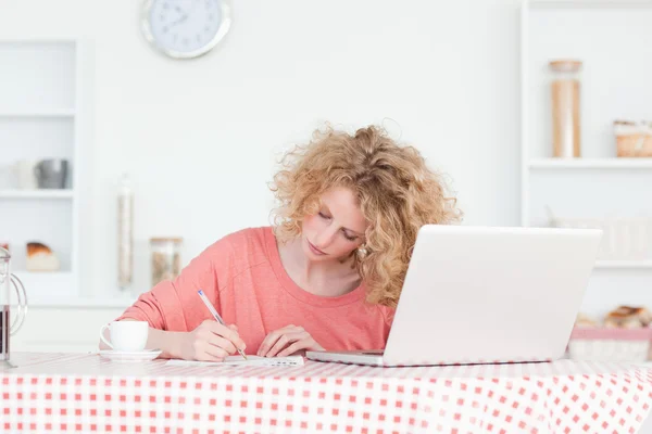 Mulher loira bonita escrevendo enquanto trabalhava com seu laptop em — Fotografia de Stock
