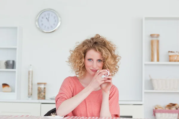 Mujer rubia guapa bebiendo una taza de café mientras está sentada —  Fotos de Stock