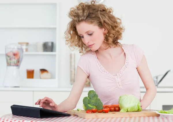 Pretty blonde woman relaxing with her tablet while cooking some — Stock Photo, Image