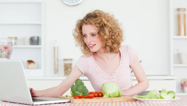 Snygg blond kvinna avkopplande med sin laptop medan matlagning — Stockfoto