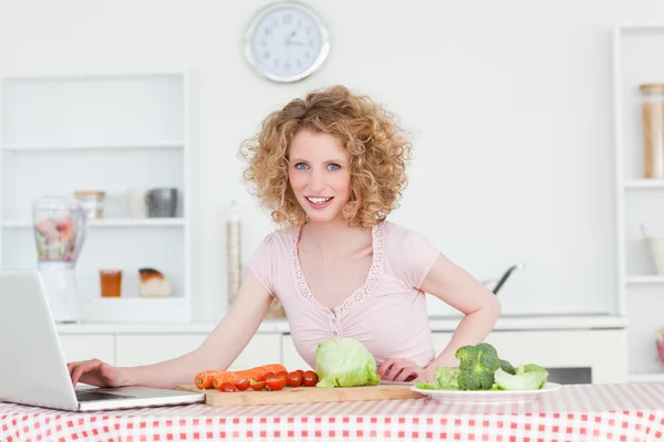 Vacker blond kvinna avkopplande med sin laptop medan matlagning så — Stockfoto