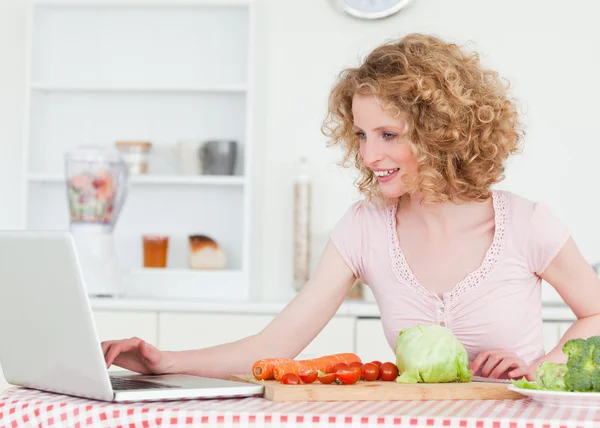 Attraktiv blond kvinna avkopplande med sin laptop medan matlagning s — Stockfoto