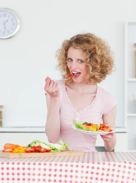Mujer rubia encantadora comiendo algunas verduras en la cocina —  Fotos de Stock