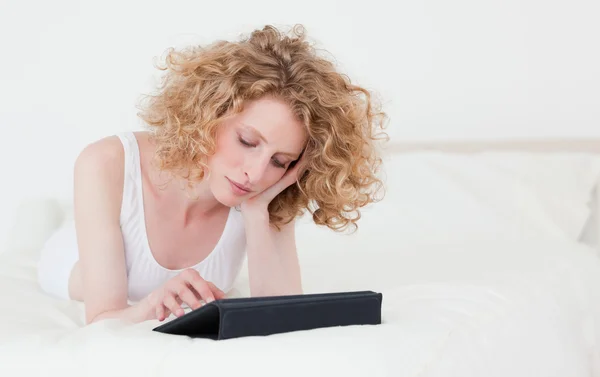 Mulher loira bonita relaxando com seu tablet enquanto deitado em um — Fotografia de Stock