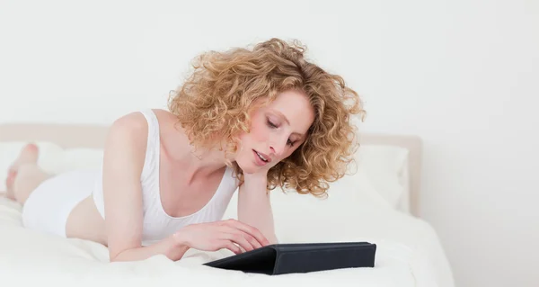 Mulher loira bonita relaxando com seu tablet enquanto deitado o — Fotografia de Stock