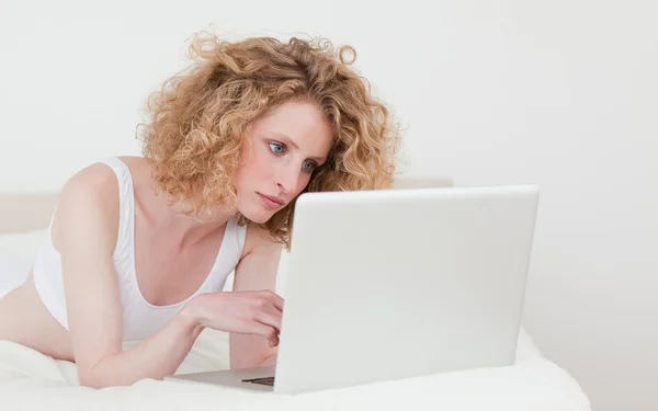 Mulher loira bonita relaxante com seu laptop enquanto deitado em h — Fotografia de Stock