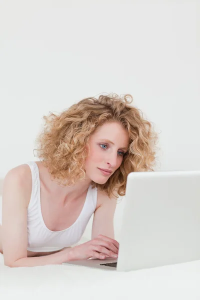 Przepiękny blond kobieta relaksując się przy jej laptop leżąc na h — Zdjęcie stockowe