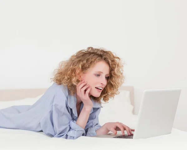 Mulher loira bonita relaxante com seu laptop enquanto deitada — Fotografia de Stock