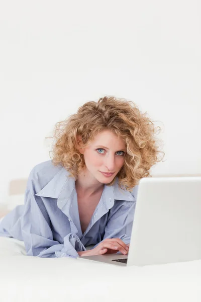 Gut aussehende blonde Frau entspannt sich im Liegen mit ihrem Laptop — Stockfoto